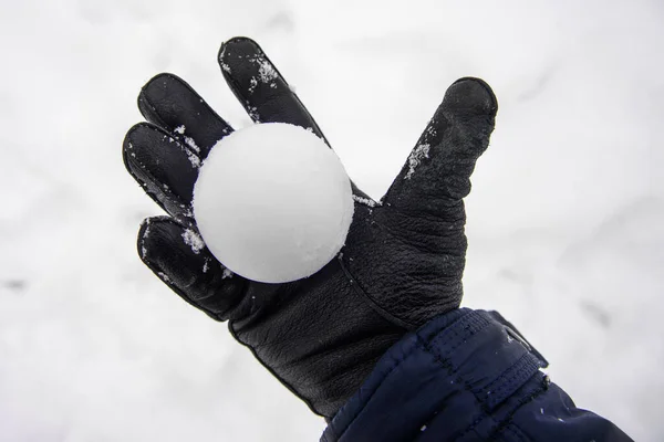 Bola de nieve en la mano. una mano en un guante sostiene una bola de nieve —  Fotos de Stock