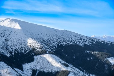 Güneş ışığı ve gölgeler ufuktaki uzak tepelerle karlı tepeleri vurgular