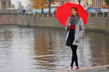 Güzel, yalnız kız şehir kanal dolgu strolling bir kırmızı şemsiye ile