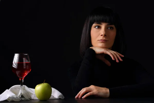 Portrait of a beautiful young woman at the moment of waiting with a glass of red wine on a dark background