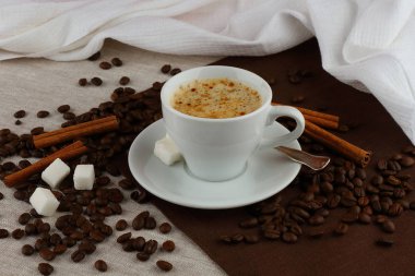 Kahve, kahve çekirdekleri ve tarçın keten peçeteler üzerinde beyaz bir fincan ile natürmort