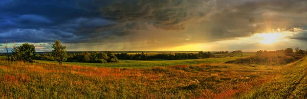 Large-format panorama of the picturesque summer landscape with the last rays of the sun before the storm