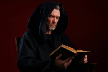 Bir ortaçağ keşiş gönüllülük a kitap bordo arka plan kukuleta ile siyah elbise içinde portresi