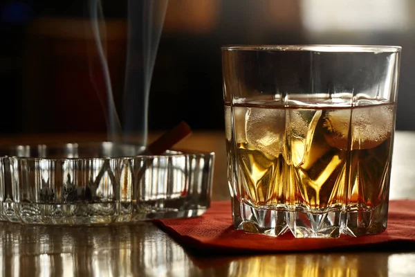 Un vaso de whisky en las rocas y un cigarrillo humeante — Foto de Stock