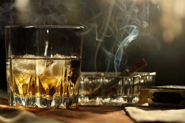 Ένα ποτήρι ουίσκι με πάγο και ένα τσιγάρο που καπνίζει — Φωτογραφία Αρχείου