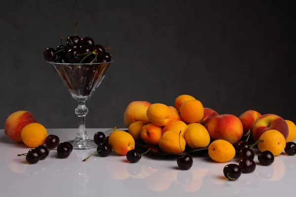 Natureza morta com cerejas, pêssegos e damascos em um backgro cinza — Fotografia de Stock