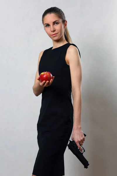 Hermosa chica en vestido negro con pistola y Apple — Foto de Stock