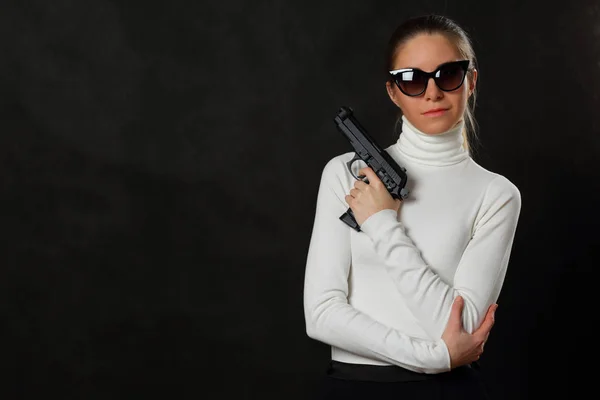 Meisje in witte trui met pistool op donkere achtergrond — Stockfoto