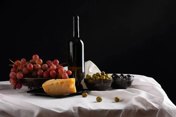 Botella de vino, aceitunas, uvas y queso sobre fondo oscuro — Foto de Stock