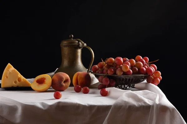 Um vaso de uvas, pêssegos, queijo e um jarro velho — Fotografia de Stock