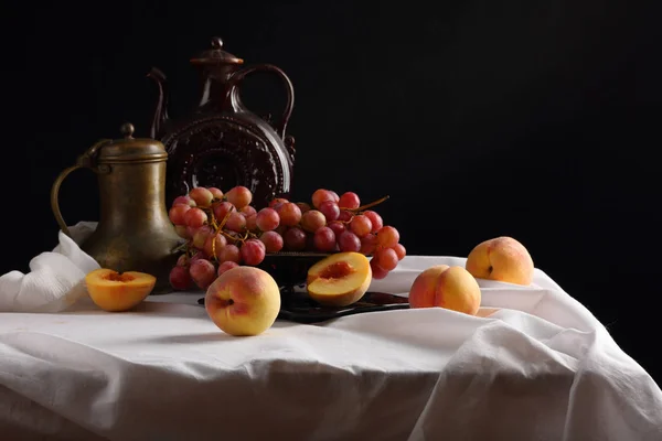 Pêssegos, uvas e jarros vintage em uma toalha de mesa branca — Fotografia de Stock