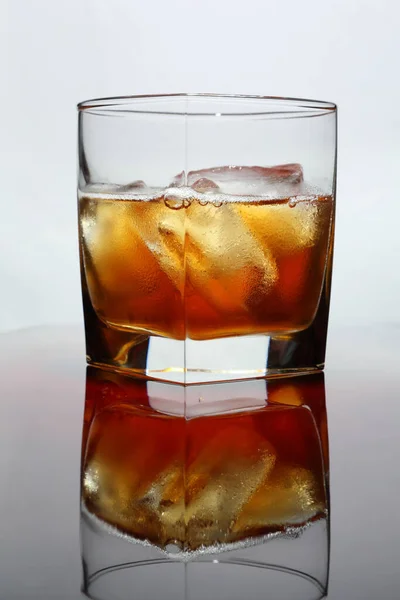 光沢のあるテーブルの上に氷のあるウイスキーのガラスと光の背景 — ストック写真