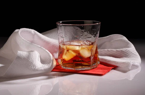白いタオルに対して光沢のあるテーブルの上に氷とウイスキーのガラス — ストック写真