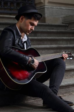 Gitarlı genç bir müzisyen eski bir binanın merdivenlerinde oturur.