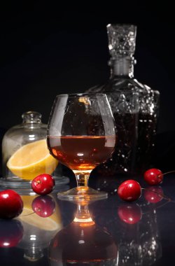 Bir bardak konyak, kiraz çileği, limon ve sürahi parlak bir masa ve koyu bir arkaplanda.