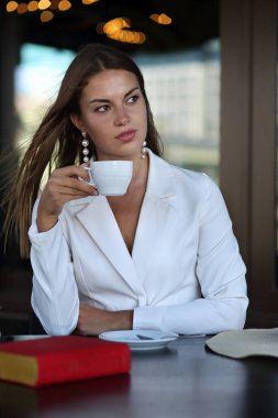 Güzel bir kız, elinde bir fincan kahve ve bir kitapla bir kafede oturuyor.