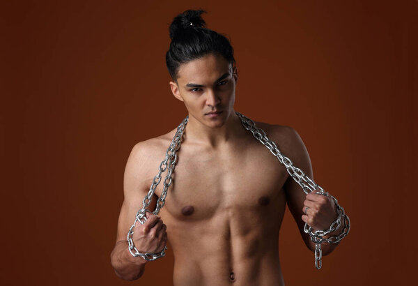 A young man of Asian appearance with a naked torso and a chain in his hands on a brown background