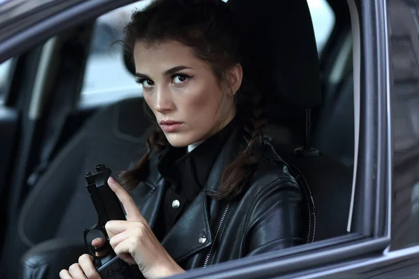 革のジャケットの美しい少女の肖像画彼女の手に銃で車を運転 — ストック写真