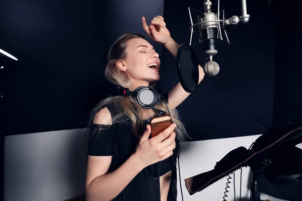 Создай что-нибудь новое! Портрет привлекательной молодой женщины с мобильным телефоном, записывающей песню в музыкальной студии . — стоковое фото
