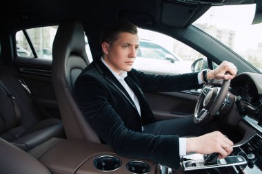 Gerçek işadamı! Yan görünümü arabada oturan ve büyük modern ofisine sürüş yakışıklı acımasız ciddi genç işadamı portresi.