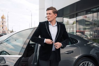 Zamanında gel! Yakışıklı ciddi genç girişimci kadar gidiş modern arabasından ise sade ceketinin düğmelerini.