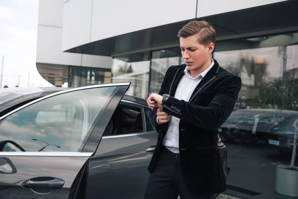 ¡No te apresures! Atractivo joven empresario inteligente comprobar el tiempo, mientras que de pie y esperando a alguien cerca del automóvil . — Foto de Stock