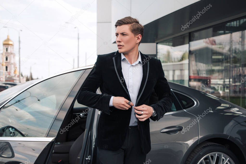 Come in time! Handsome serious young entrepreneur buttoning his understated jacket, while going out of his modern car.