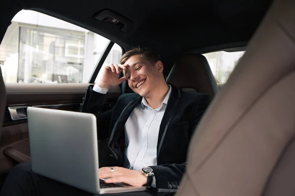 ¡Sé siempre alegre y positivo! Alegre reconocido joven empresario profesional sentado en el coche y sonriendo, mientras trabajaba en el portátil . — Foto de Stock