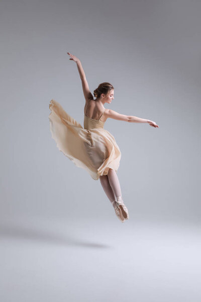 Moment when you feel alive! Young graceful woman ballet dancer, dressed in professional outfit, shoes and beige weightless skirt demonstrating her dancing skills.
