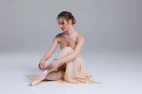 Enjoy your relaxation! Side view portrait of the young ballerina sitting on the floor in the modern dancing studio and posing at the camera. — Stock Photo, Image