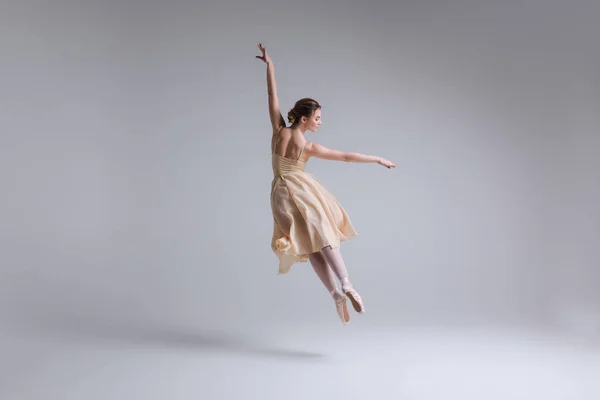 Express yourself! Beautiful tender female ballet dancer with flowing beige fabric dress dancing with grace in the isolated studio. — Stock Photo, Image