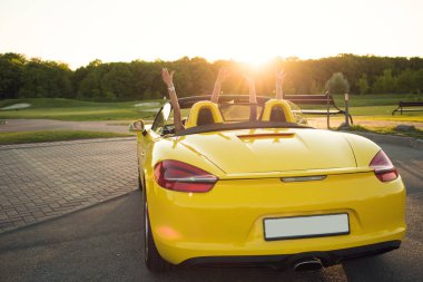 Lüks hayatın izleyin! İki genç zengin şık kız ellerini yukarı doğru güneş cabrio içinde otururken yükselterek görünümü fotoğraf geri. 