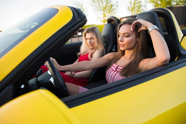 Les femmes cadres ! Gros plan portrait de deux sexy belle fille tendre conduisant l'automobile jaune à l'heure d'été . Images De Stock Libres De Droits