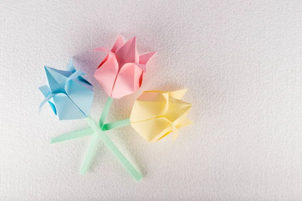Three origami flowers on white textured background
