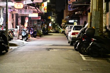 Taipei, Tayvan - Nisan. 04, 2025: Gizli Tayvan sokak sahnesi geceleri park halindeki motorlu scooterlar, bitkisel çaycı tabelası, çevredeki sokak ışıklarıyla tipik bir Taipei sokağı gösteriyor.