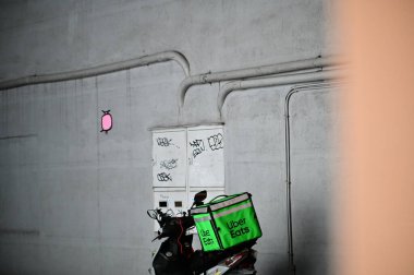 Taipei, Tayvan - Nisan. 04, 2025: Uber Eats markalı yeşil termal dağıtım çantasının besin dağıtım ekipmanlarını gösteren beton duvara monte edilmiş belgesel fotoğrafı.