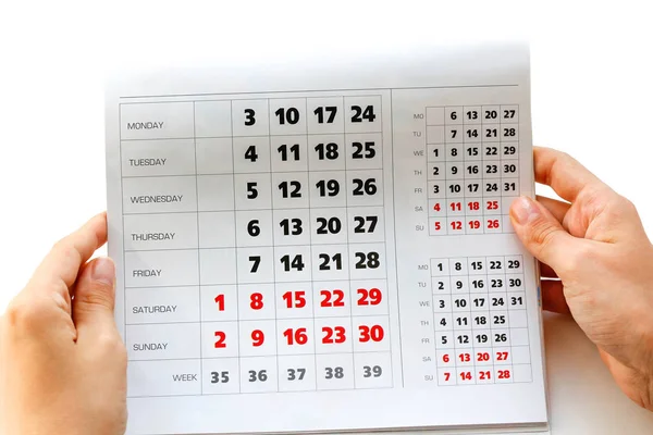 Hand holding the calendar. White calendar. Weekends are highlighted in red. Close up