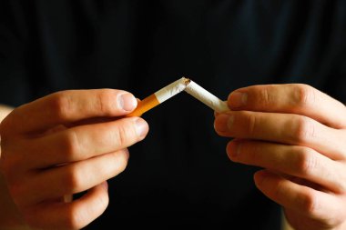 Bir adam kırık bir sigara elinde tutuyor. Yakın çekim. İzole arka plan.