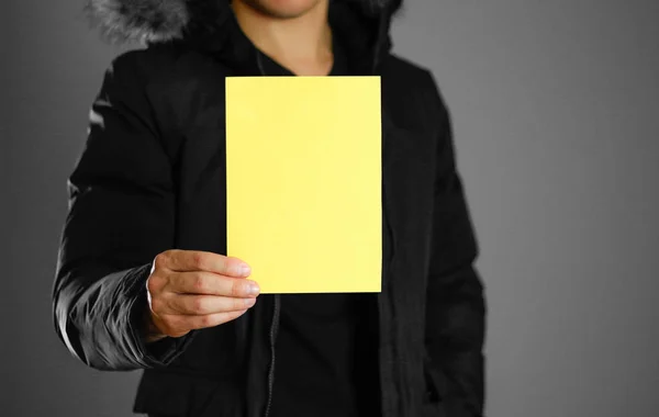 一个穿着温暖的冬衣的男人拿着一张黄色的传单 空白纸张 闭上你的嘴隔离的背景 — 图库照片