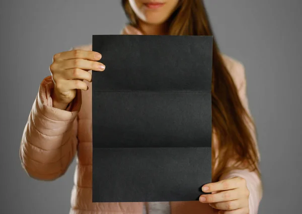 一个穿着温暖的冬衣的女人拿着一张黑色的传单 空白纸张 闭上你的嘴隔离的背景 — 图库照片