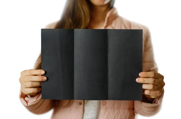 一个穿着温暖的冬衣的女人拿着一张黑色的传单 空白纸张 闭上你的嘴隔离在白色背景上 — 图库照片