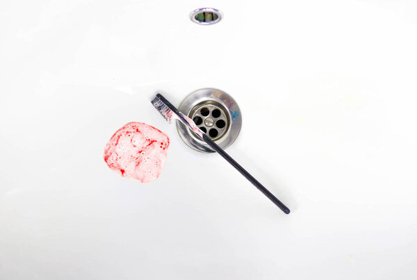 Toothpaste with blood in a ceramic sink. Bleeding gums. Close up.