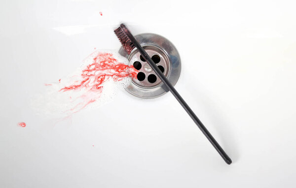 Toothpaste with blood in a ceramic sink. Bleeding gums. Close up.