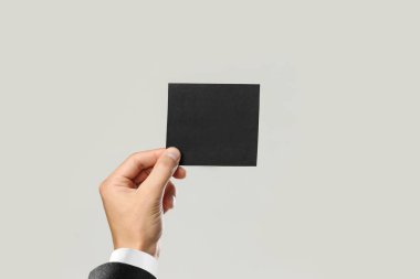 Beyaz gömlek ve siyah ceket siyah parça kağıt tutan erkek elinde. Gri arka plan üzerinde izole. Portre.