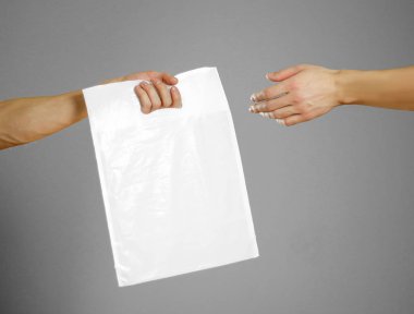Bir erkek eli beyaz bir plastik torba geçer. Yakın çekim. Gri arka plan üzerinde izole.