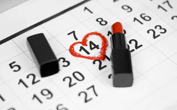 Valentines day and Holidays concept. Calendar sheet with 14th february date marked by red heart shape with red lipstick. Close up.