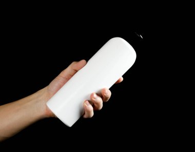 Beyaz şampuanı şişe tutan el. Yakın çekim. Siyah arka plan üzerine izole.