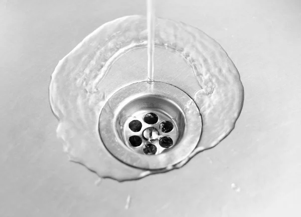 Water runs into the drain hole in the metal sink. Close up — Stock Photo, Image