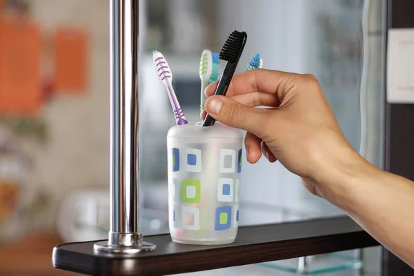 Hand takes a toothbrush from a plastic cup. One brush stands out — Stock Photo, Image