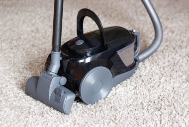 Güzel bir siyah elektrik süpürgesi ile bej halı üzerinde duruyor